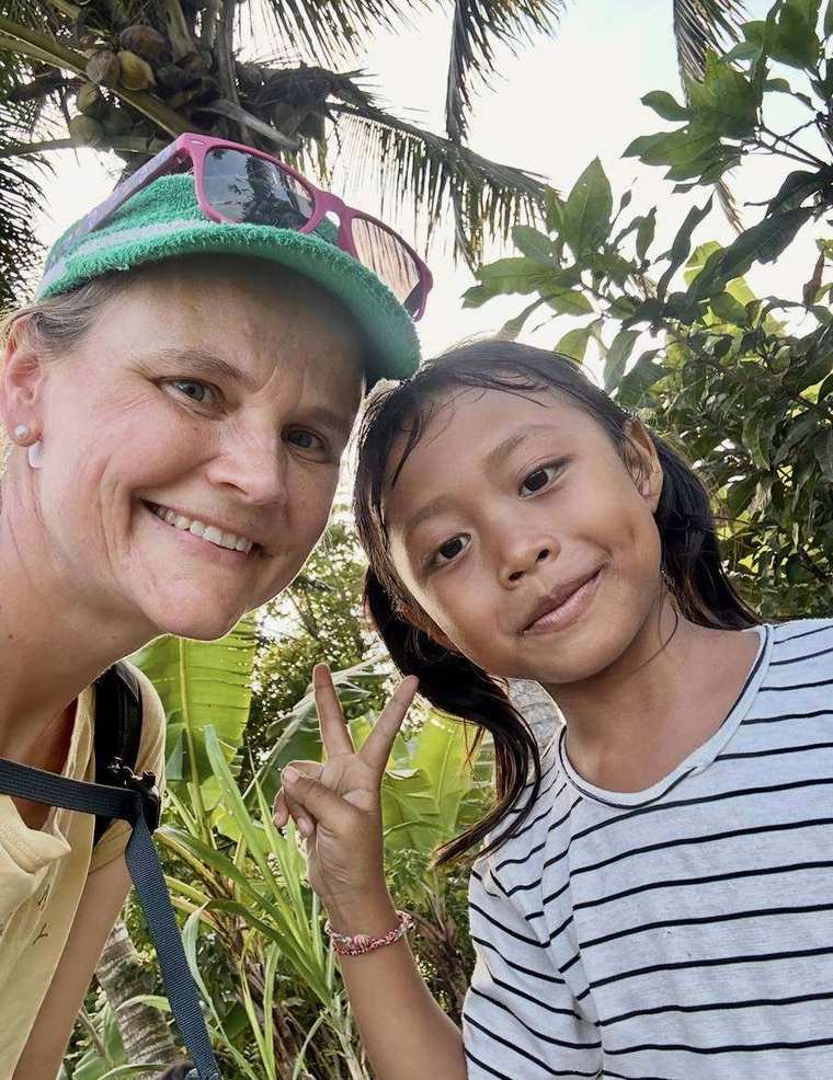 Christin lächelnd bei einem Selfie mit einem Mädchen unter Palmen