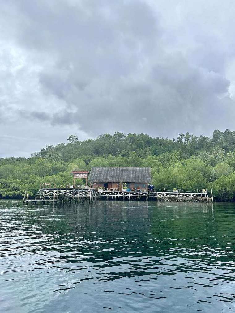 Das Schulgebäude von Child Aid Papua steht auf Stelzen am Wasser vor bewaldeten Hügeln